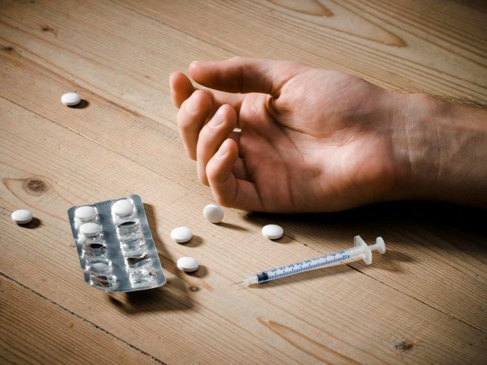 Hand of a drug addict with syringe and pills lying on a wooden floor