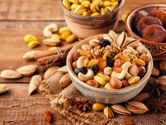Bowls filled with dry fruits (raisins, pistachios, apricots, cashews, almonds, and walnuts) on a wooden table