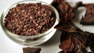 Close-up of a bowl of dried dulse seaweed flakes and whole plant on a white table