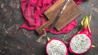 Dragon fruit cut into half next to a wooden board and knife on a red fabric