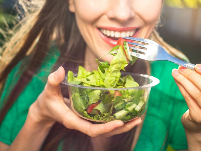A woman happily eating green salad