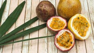 Whole and sliced passion fruit with leaves on a light wooden table