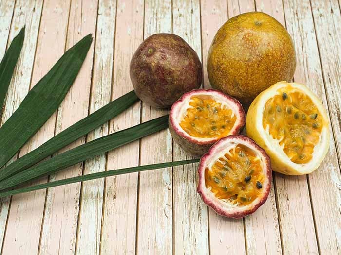 Whole and sliced passion fruit with leaves on a light wooden table