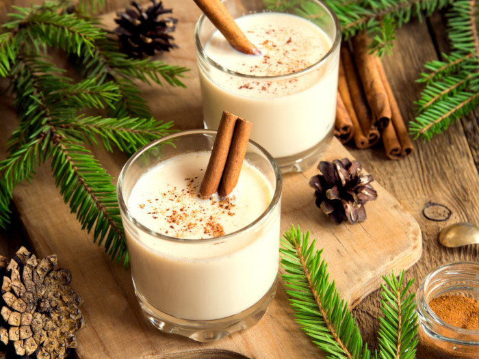 Eggnog in two glasses garnished with cinnamon sticks, in a festive setting