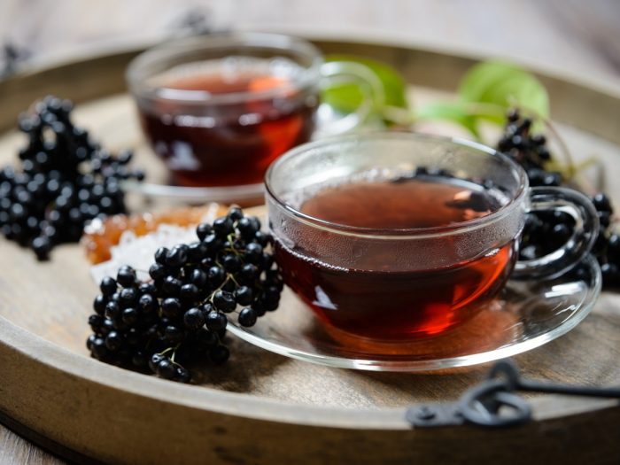 Cups of elderberry tea with fresh elderberries on a wooden table