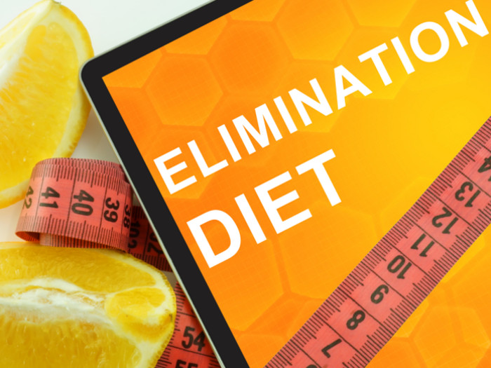 A board with 'elimination diet' written on it next to a measuring tape and orange slices