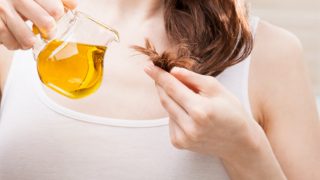 Girl holding the ends of her hair to a bottle of oil held in the other hand