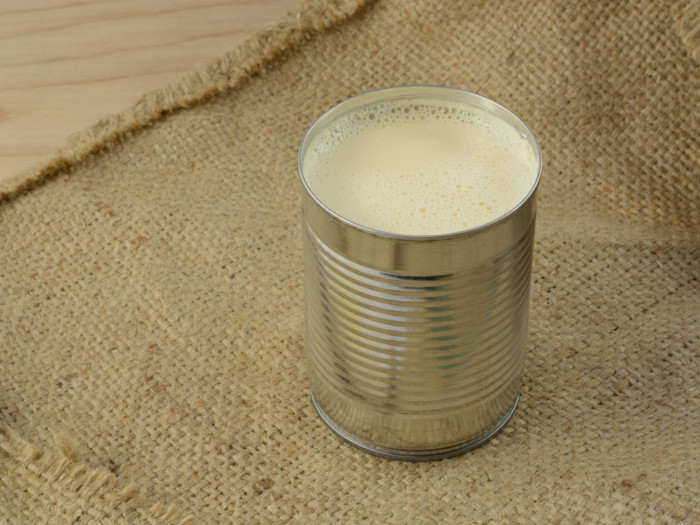 Open tin of evaporated milk placed on burlap cloth.