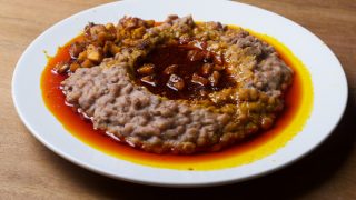 Ewa agoyin plate of mashed beans with diced fried plantain and red palm oil stew on a wooden counter