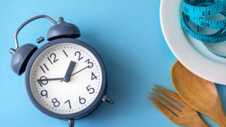 alarm clock, plate, measuring tape, spoon and fork laid out on a measuring table
