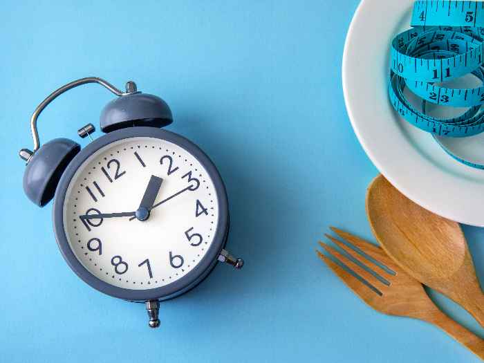Alarm clock, plate, measuring tape, spoon and fork laid out on a measuring table