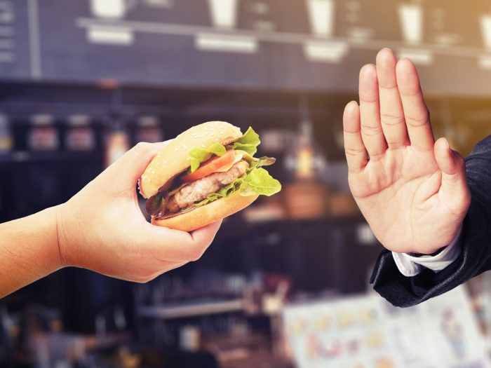 A man is offering a delicious burger to another man said no during the fast in the coffee shop