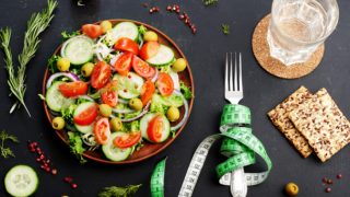 Flatline view of a salad, biscuits, a glass of water and fork wrapped up in a tape measure, on a slate background.