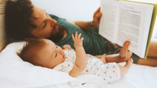A father reading a book to a baby while laying on the bed