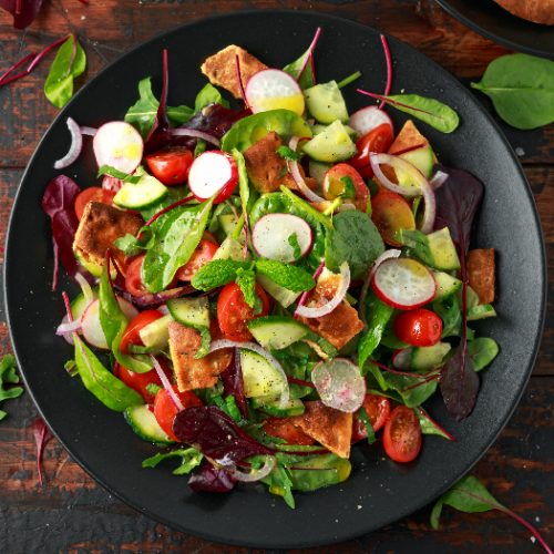 Traditional fattoush salad on a plate with pita croutons, cucumber, tomato, red onion, vegetables mix and herbs