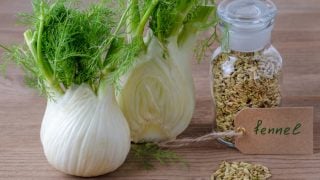 2 fresh fennel bulbs and a jar of fennel seeds on a wooden table