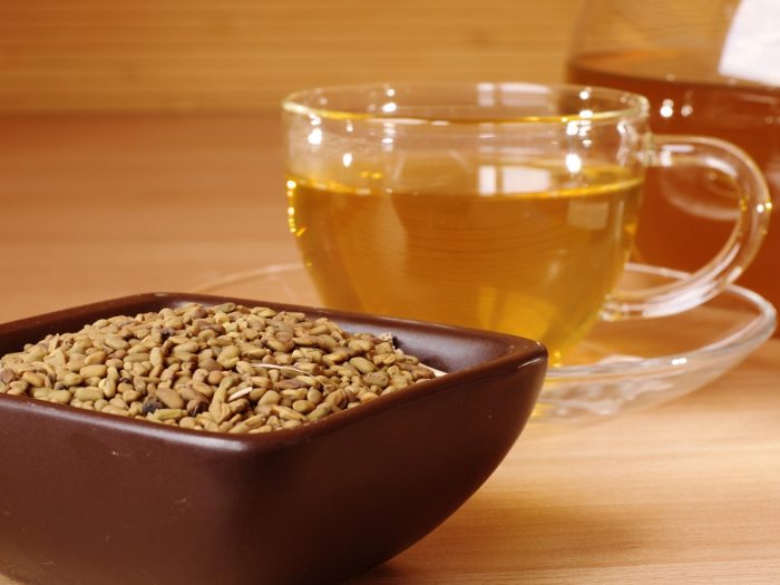 A bowl of fenugreek seeds with a cup of tea on a wooden table