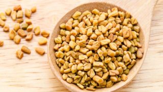 A wooden spoon filled with fenugreek seeds placed on a wooden table