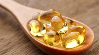 Fish oil yellow capsules on a wooden spoon on a wooden counter
