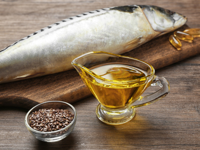 Raw fish, fish oil capsules, flaxseeds, and flaxseed oil on a wooden board