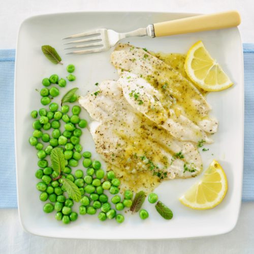 A top view of fish fillets drizzled with lemon butter sauce and organic minty peas