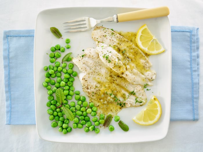 A top view of fish fillets drizzled with lemon butter sauce and organic minty peas