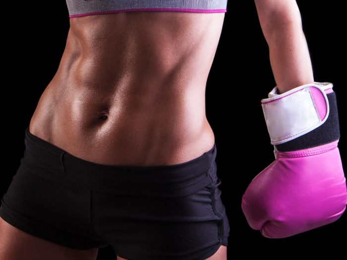 A fit woman showing flat tummy and one hand covered with wrestling glove