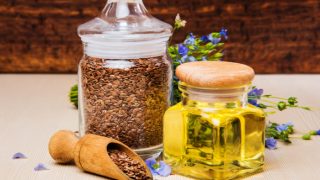 A small glass jar of flaxseed oil kept next to a jar of flaxseeds