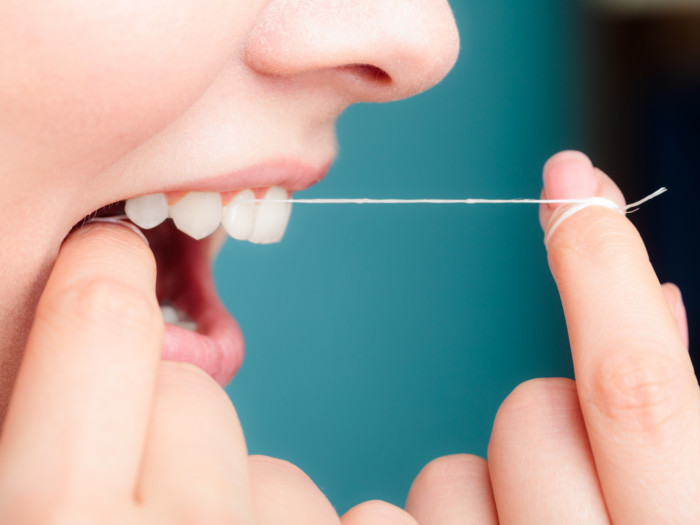 Profile view of a woman flossing her teeth.