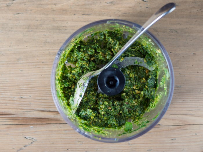 A close-up shot of spoon in a food processor filled with pesto