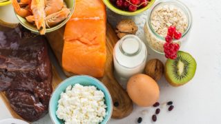 Flatlay picture of liver, fish, shrimps, egg, milk, fish, nuts, cheese, berries, and oats.