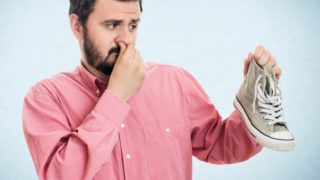 A man holding his shoes in his hand while pinching his nose at the same time
