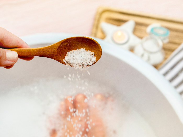 Adding salts in foot bath water with foot soak materials in the background