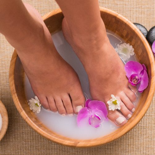 Woman soaking her feet in dish with orchids and white flowers in the spa water