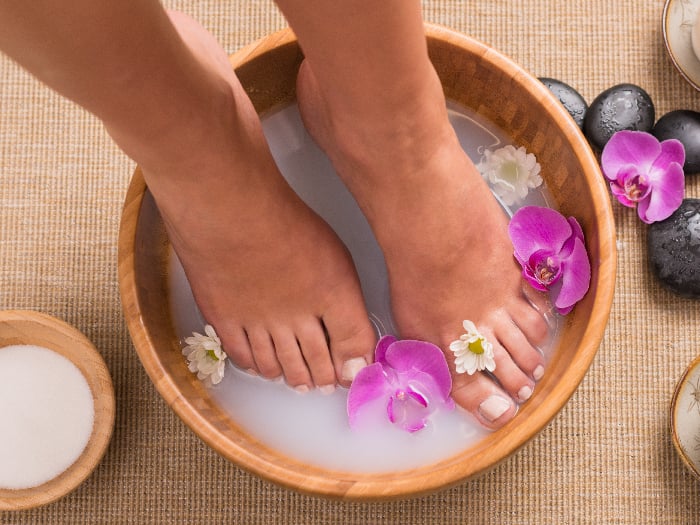 Woman soaking her feet in dish with orchids and white flowers in the spa water