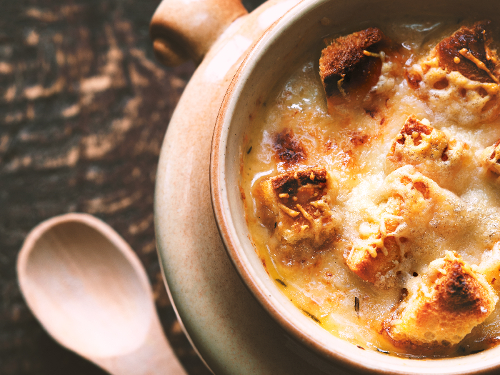 A close up shot of onion soup in a ceramic pot placed on a wooden table