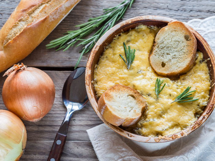 A close up shot of a bowl of onion soup kept on the wooden table