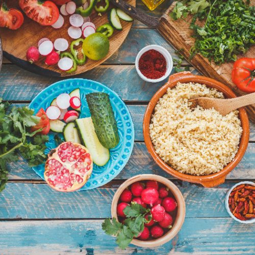 Various fresh vegetables on a blue wooden table and cook burghul in ceramic bowl