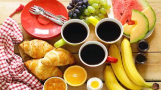 A breakfast platter consisting of bananas, egg, croissants, sliced watermelon, grapes, and black coffee