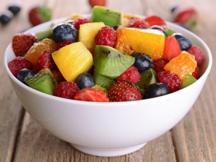 A bowl of sliced berries and fruits on a wooden counter