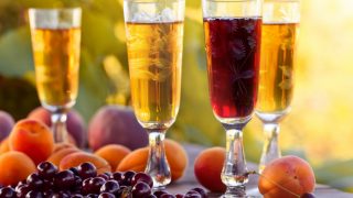Yellow and red fruit wine in beautiful glasses next to peaches and cranberries