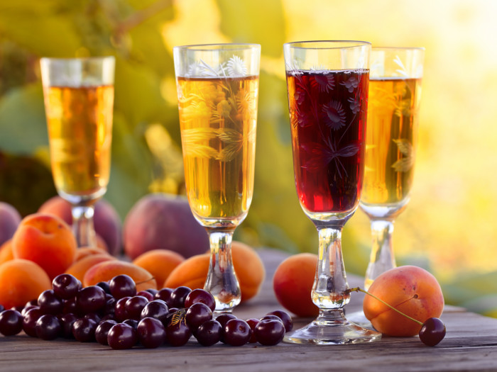 Yellow and red fruit wine in beautiful glasses next to peaches and cranberries