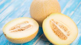 Close-up of fresh whole and halved galia melons on a blue wooden table