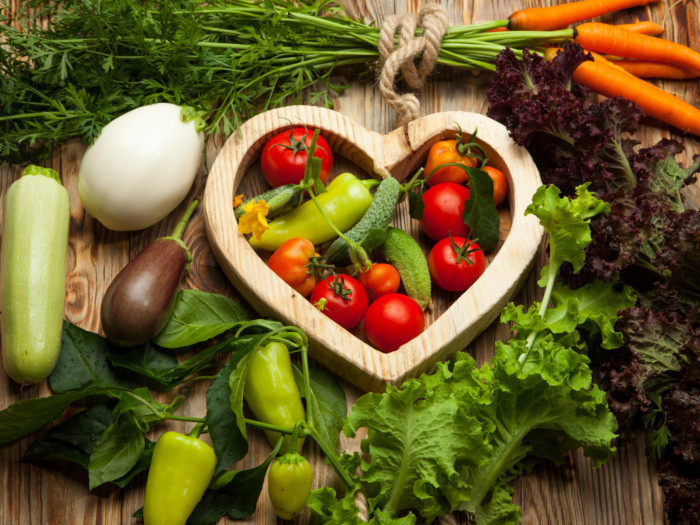 Different vegetables lying on a wooden table with a wooden heart in the center