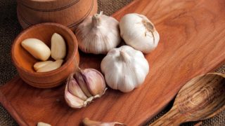 Sliced garlic, garlic clove, garlic bulb in a wooden bowl placed on a chopping board
