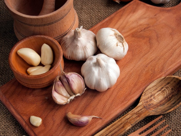 Sliced garlic, garlic clove, garlic bulb in a wooden bowl placed on a chopping board