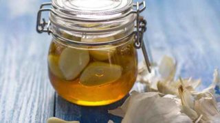 A glass container with garlic cloves in honey, and whole garlic cloves next t it