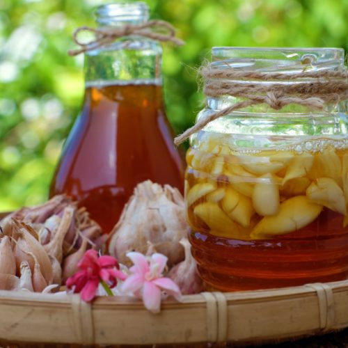 Jars of honey and garlic soaked in honey in a basket with garlic and flowers