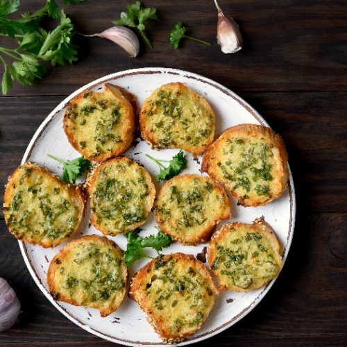 Cheese garlic bread with green herbs on plate over wooden background