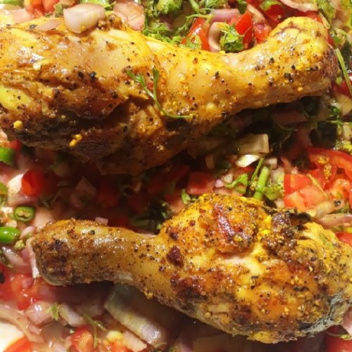 Spice-coated chicken on a bed of tomato onion salad garnished with lemon